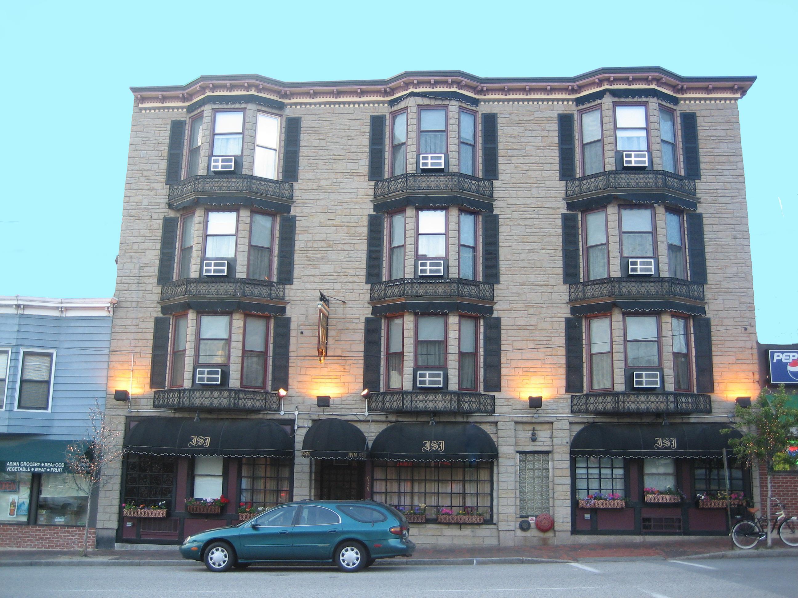 A building with 9 bay waved windows subdivided into 6 panes each. The lower middle pane of each has an air conditioning. A long blue sedan or hatchback is parked in front of the building. Not a lot more to it. Portland, Maine, June 2008. Photo by Peachfront.