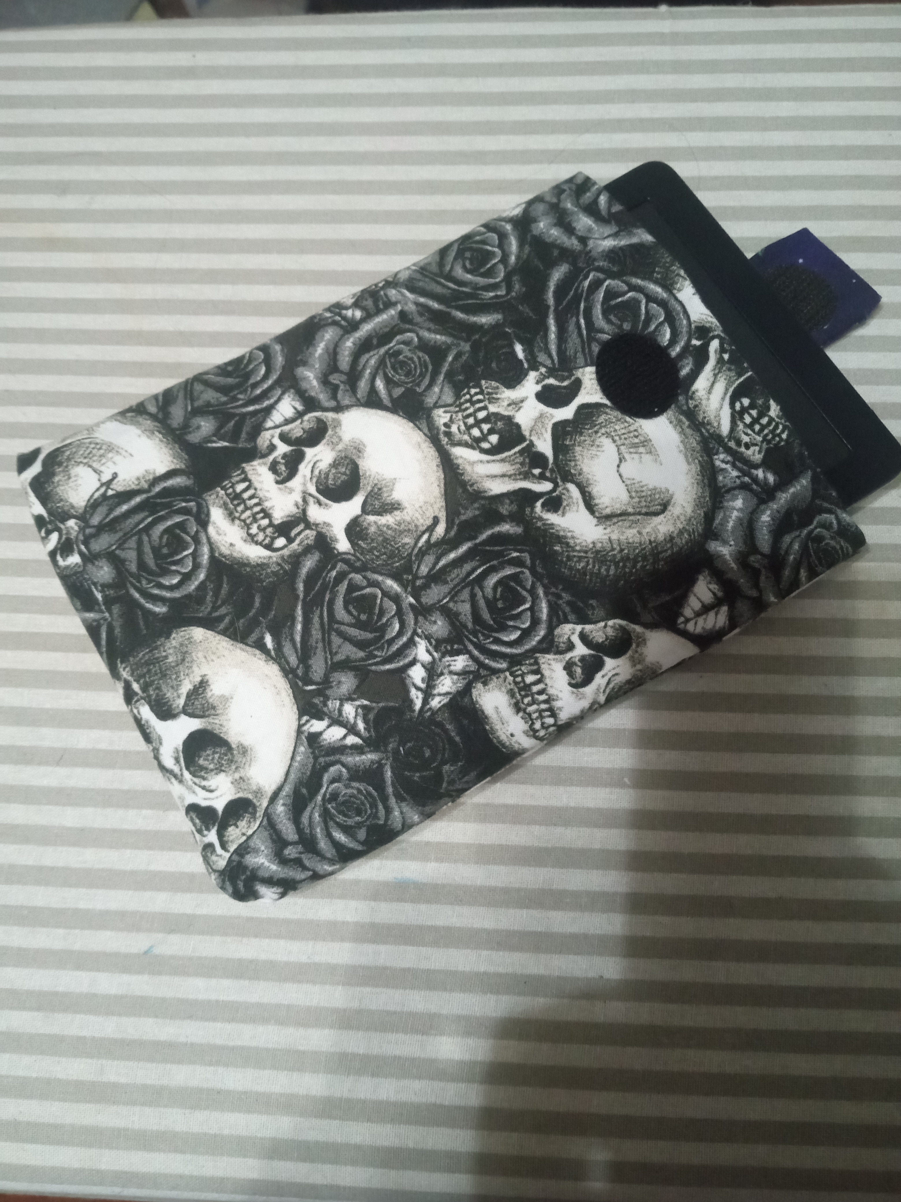 rectangular cloth case made of fabric printed with skulls and roses. there is an e-reader partially inside the case