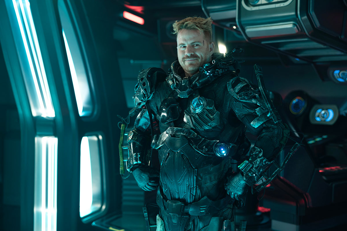 Section 31's Zeph, wearing his mech suit with his hands on his hips, with a goofy-looking grin on his face.