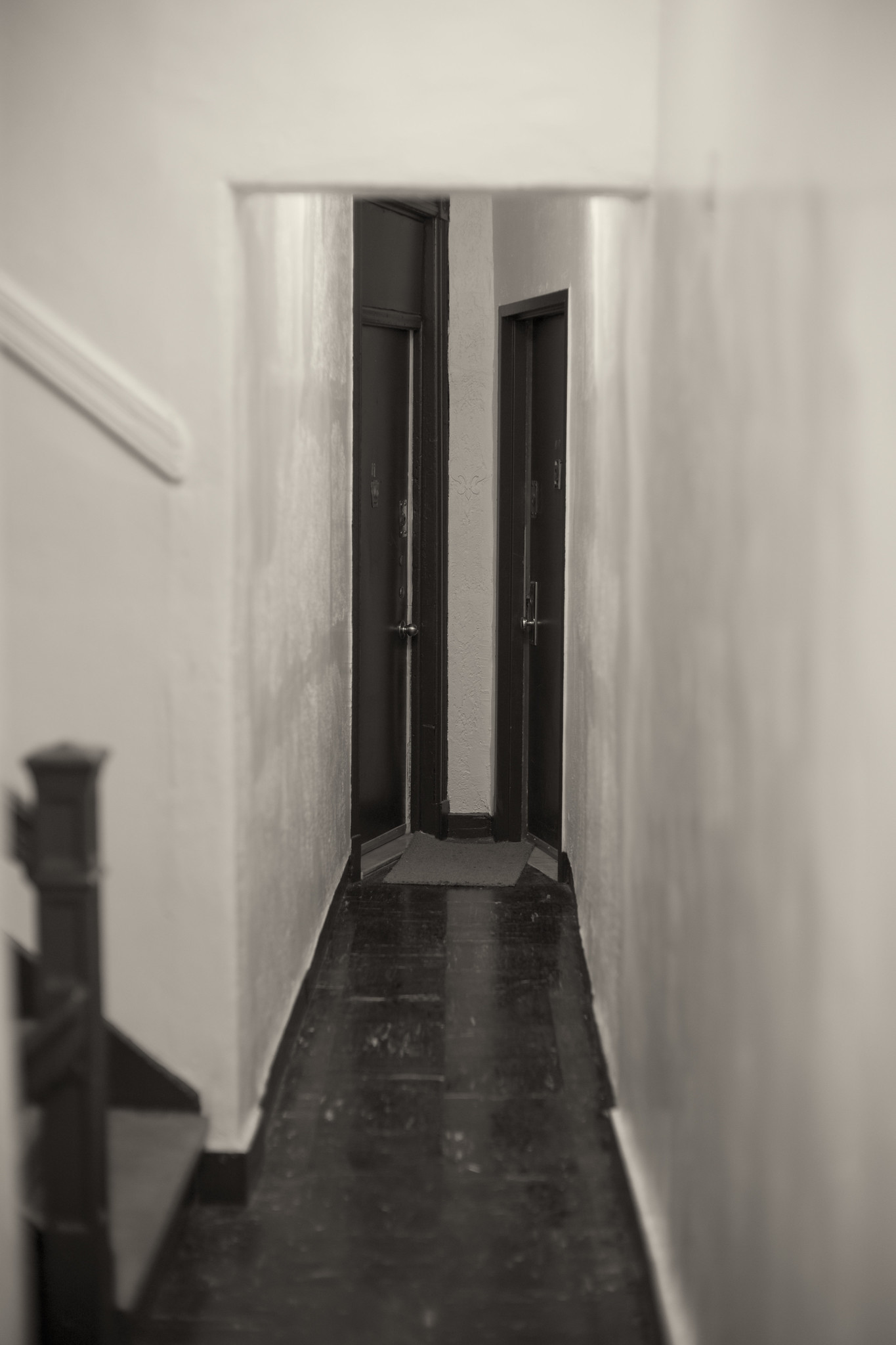 A narrow hallway in a walk-up apartment building, ending with two adjacent doors at a 90 degree angle from one another.